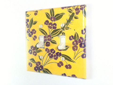 A bright yellow double toggle switch plate with dark and light plum colored flowers, green leaves, and gold details by The Orange Chair Studio.